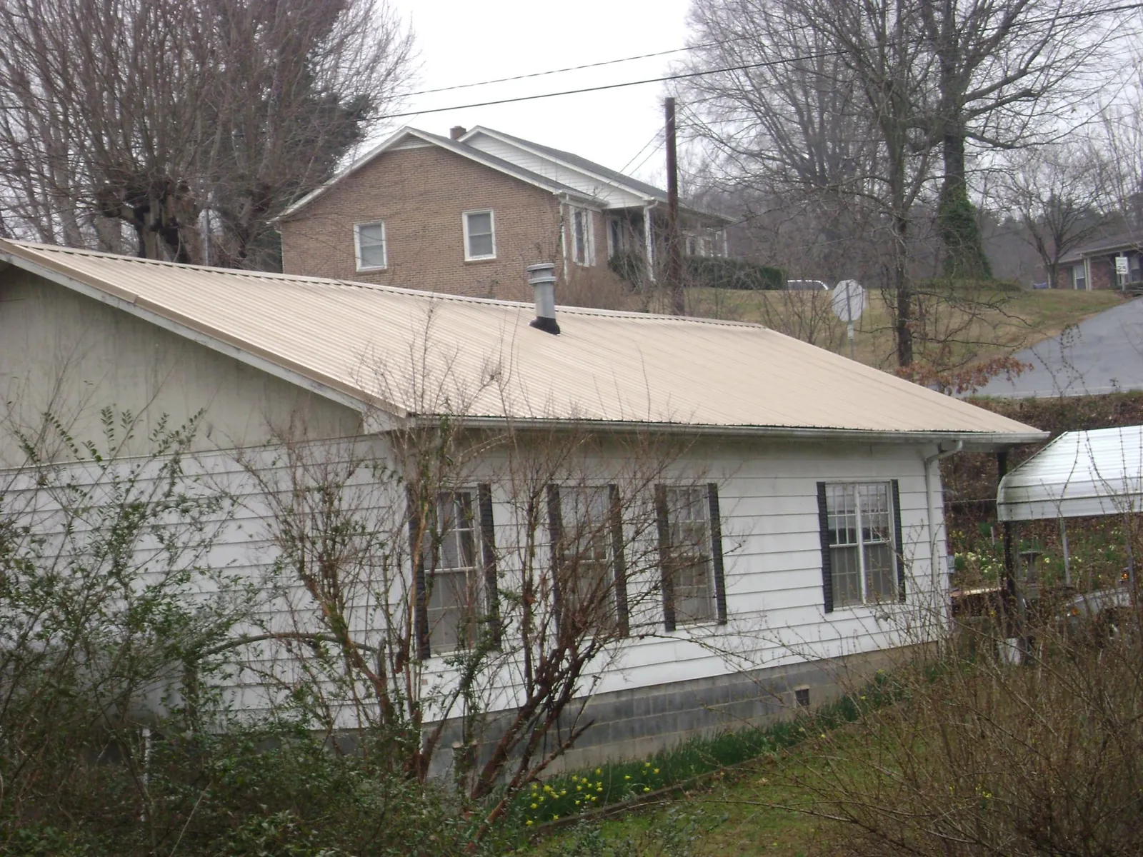 Tan metal roof on a white sided house set into a hillside — Commercial Roofing by Roofing Brothers in Sorrento